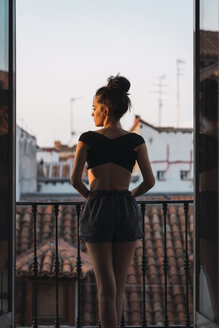 Beautiful young woman standing on balcony at sunset - KKAF01847