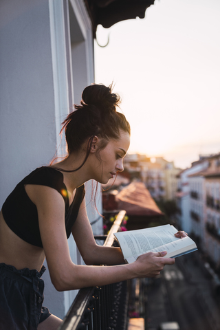Beautiful young woman on balcony above the city at sunset reading a book stock photo
