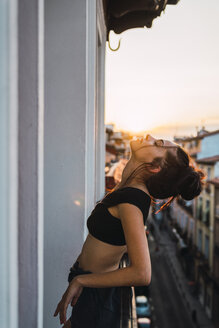 Schöne junge Frau auf Balkon über der Stadt bei Sonnenuntergang - KKAF01850