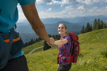 Deutschland, Bayern, Brauneck bei Lenggries, glückliche junge Frau wandert in alpiner Landschaft und hält die Hand ihres Freundes - LBF02076