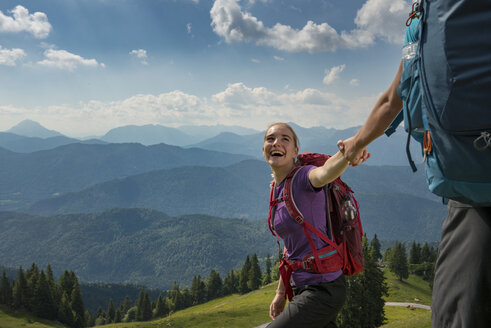 Deutschland, Bayern, Brauneck bei Lenggries, glückliche junge Frau wandert in alpiner Landschaft und hält die Hand ihres Freundes - LBF02078