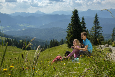 Germany, Bavaria, Brauneck near Lenggries, happy young couple having a break sitting in meadow in alpine landscape - LBF02086