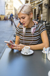 Italien, Florenz, Porträt einer jungen Frau in einem Straßencafé, die auf ihr Smartphone schaut - MGIF00244