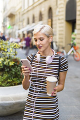 Porträt einer jungen Frau in einem gestreiften Kleid, die mit einem Kaffee auf der Straße steht und auf ihr Mobiltelefon schaut - MGIF00247