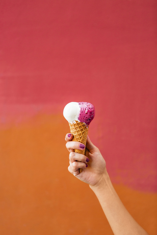 Eine Frau hält ein Eis vor einer bunten Kulisse, lizenzfreies Stockfoto