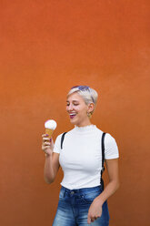 Laughing young woman with ice cream cone in front of orange background - MGIF00259
