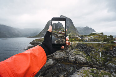 Norwegen, Lofoten, Männerhand beim Fotografieren mit dem Handy an der Küste - KKAF01864