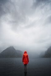 Norway, Lofoten, rear view of man standing on a pole at the coast - KKAF01875