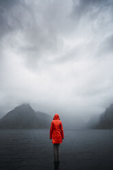 Norwegen, Lofoten, Rückansicht eines Mannes, der auf einem Pfahl an der Küste steht - KKAF01875