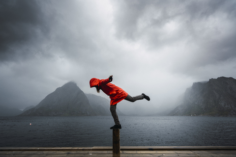 Norwegen, Lofoten, Mann balanciert auf einer Stange an der Küste, lizenzfreies Stockfoto