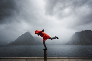 Norwegen, Lofoten, Mann balanciert auf einer Stange an der Küste - KKAF01878