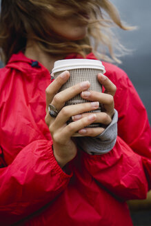 Norwegen, Lofoten, Nahaufnahme einer jungen Frau an der Küste mit Kaffee zum Mitnehmen - KKAF01883