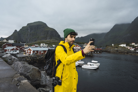 Norwegen, Lofoten, junger Mann in einem Fischerdorf an der Küste macht ein Selfie, lizenzfreies Stockfoto