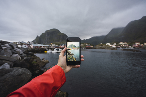 Norwegen, Lofoten, Männerhand beim Fotografieren mit dem Handy an der Küste, lizenzfreies Stockfoto