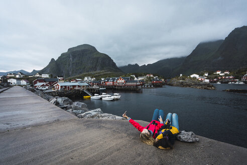 Norwegen, Lofoten, zwei junge Frauen liegen auf einem Pier an der Küste und machen ein Selfie - KKAF01888