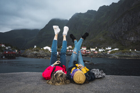 Norwegen, Lofoten, zwei junge Frauen liegen auf einem Pier an der Küste - KKAF01889