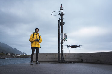 Norwegen, Lofoten, Mann steht an der Küste und fliegt eine Drohne - KKAF01896