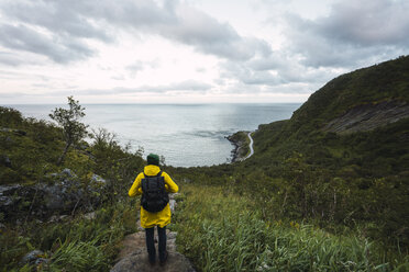 Norway, Lofoten, rear view of man standing on coastal path - KKAF01897