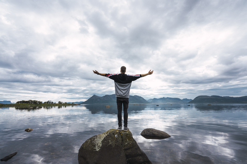 Norwegen, Insel Senja, Rückansicht eines Mannes, der auf einem Felsen an der Küste steht, lizenzfreies Stockfoto