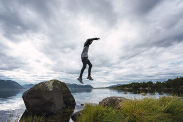 Norwegen, Insel Senja, Mann springt von einem Felsen an der Küste - KKAF01902