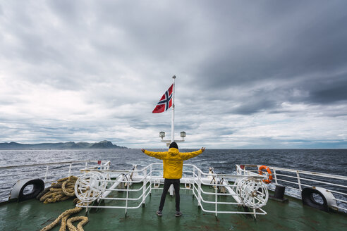 Norwegen, Insel Senja, Rückansicht eines auf dem Schiffsdeck stehenden Mannes mit ausgestreckten Armen - KKAF01903
