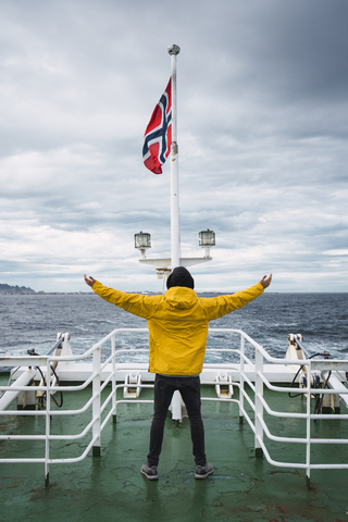 Norway, Senja island, rear view of man standing on ship deck with outstretched arms stock photo