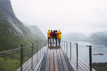 Norwegen, Insel Senja, Rückansicht von Freunden, die auf einer Aussichtsplattform an der Küste stehen - KKAF01906