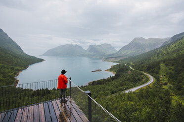 Norwegen, Insel Senja, Rückansicht eines Mannes, der auf einer Aussichtsplattform an der Küste steht - KKAF01909