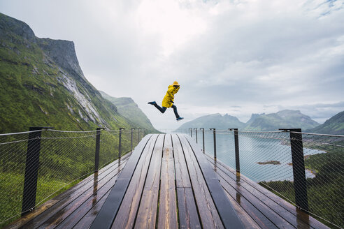 Norwegen, Insel Senja, Mann springt auf eine Aussichtsplattform an der Küste - KKAF01911