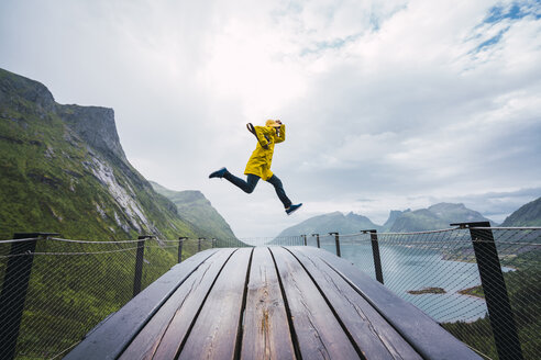 Norwegen, Insel Senja, Mann springt auf eine Aussichtsplattform an der Küste - KKAF01912