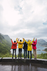 Norwegen, Insel Senja, Rückansicht von jubelnden Freunden, die auf einem Aussichtspunkt an der Küste stehen - KKAF01914