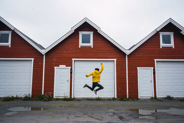 Norwegen, Mann springt vor eine Reihe von Hütten - KKAF01920