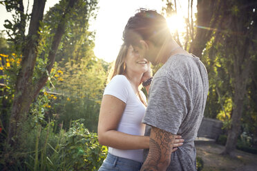 Glückliches junges Paar umarmt und küsst sich in einem Park im Sommer - SRYF00808
