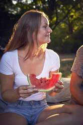 Young couple sitting in park, eating watermelon - SRYF00813