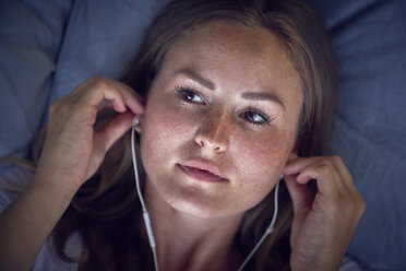 Young woman lying on cushion, listening music with earphones - SRYF00837