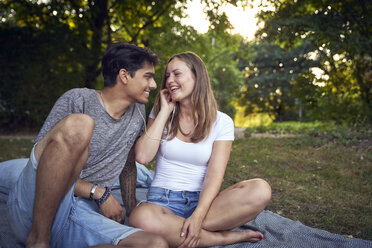 Young couple sitting in park, sharing earphones, listening music - SRYF00841