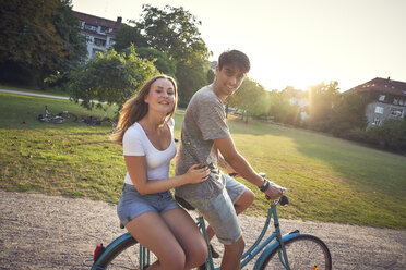 Junges Paar fährt Fahrrad im Park, Frau sitzt auf dem Gepäckträger - SRYF00846