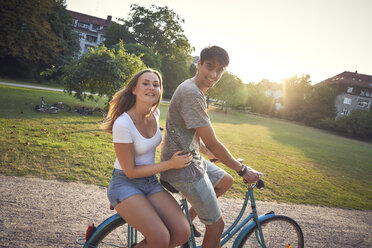 Young couple riding bicycle in park, woman sitting on rack - SRYF00846