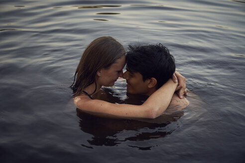 Romantisches Paar, das sich bei Sonnenuntergang im See umarmt - SRYF00858