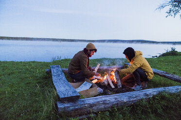 Schweden, Lappland, Zwei Freunde bereiten ein Lagerfeuer am Seeufer vor - KKAF01924