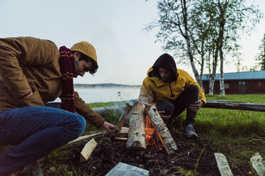 Schweden, Lappland, Zwei Freunde bereiten ein Lagerfeuer am Seeufer vor - KKAF01926