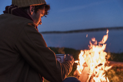 Junger Mann sitzt an einem Lagerfeuer und beobachtet die Flammen, lizenzfreies Stockfoto