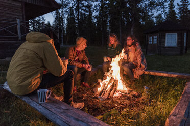 Eine Gruppe von Freunden sitzt an einem Lagerfeuer, redet und trinkt Tee - KKAF01938