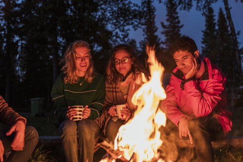 Eine Gruppe von Freunden sitzt an einem Lagerfeuer, redet und trinkt Tee - KKAF01942