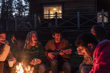 Eine Gruppe von Freunden sitzt am Lagerfeuer, redet und spielt Gitarre - KKAF01945