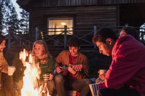 Eine Gruppe von Freunden sitzt am Lagerfeuer, redet und spielt Gitarre - KKAF01946