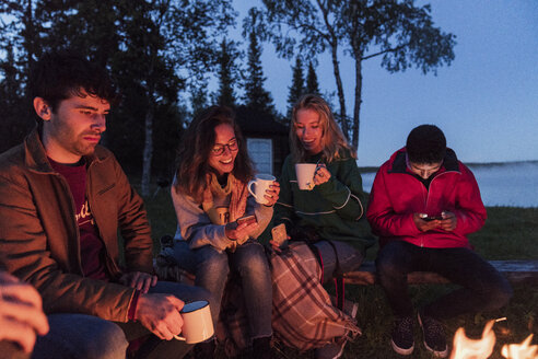 Group of friends sitting at a campfire, talking and drinking tea - KKAF01951