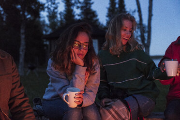 Eine Gruppe von Freunden sitzt an einem Lagerfeuer, redet und trinkt Tee - KKAF01952