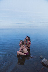 Zwei junge Frauen in Bikinis, die auf einem Stein in einem See sitzen - KKAF01953