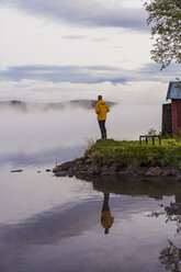 Ein einsamer Mann steht am See und schaut in den Nebel - KKAF01966